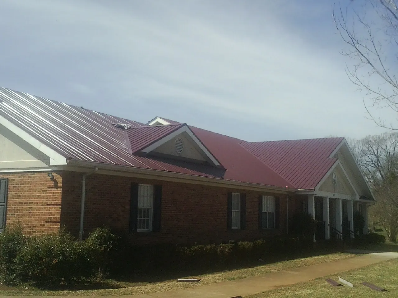Red metal roof with gabled entries on a long brick building, from a Hail Damage Roof Repair job in Longport