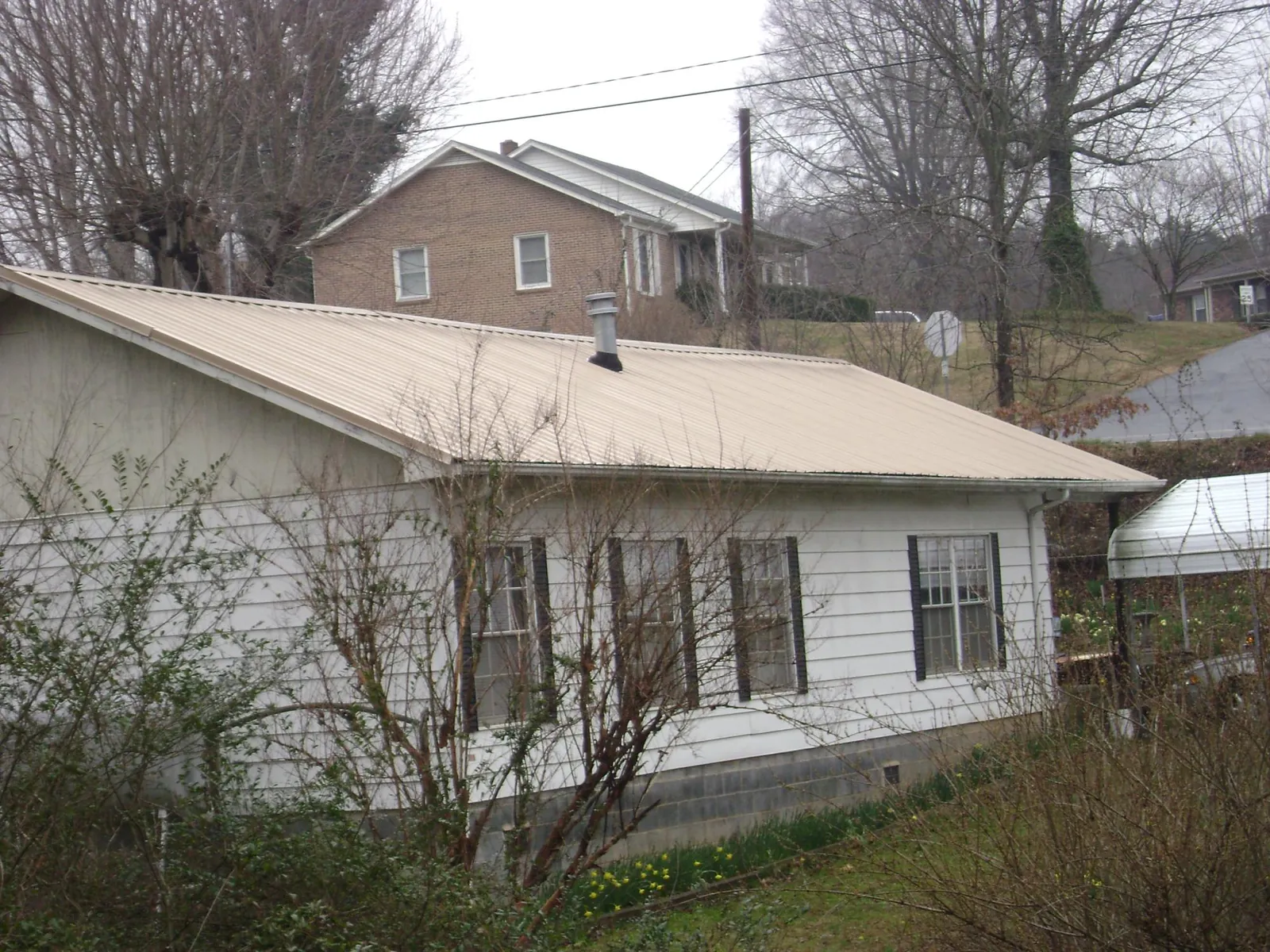 Tan metal roof on a white sided house set into a hillside — Commercial Roofing by Roofing Brothers in Longport